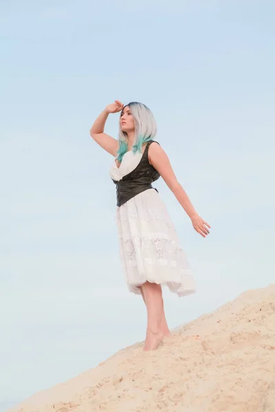 Jeune belle femme caucasienne en robe blanche et gilet en cuir marron posant dans un paysage désertique avec du sable . — Photo