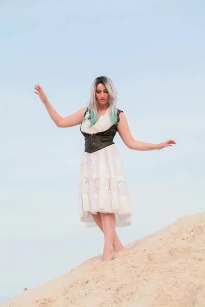 Jonge mooie blanke vrouw in witte jurk en bruin lederen gilet poseren in woestijn landschap met zand. — Stockfoto