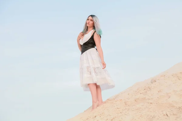 Молодая красивая кавказская женщина в белом платье и коричневом кожаном жилете позирует в пустынном пейзаже с песком . — стоковое фото