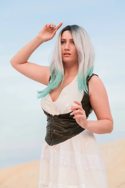 Jovem mulher branca bonita em vestido branco e colete de couro marrom posando na paisagem do deserto com areia . — Fotografia de Stock