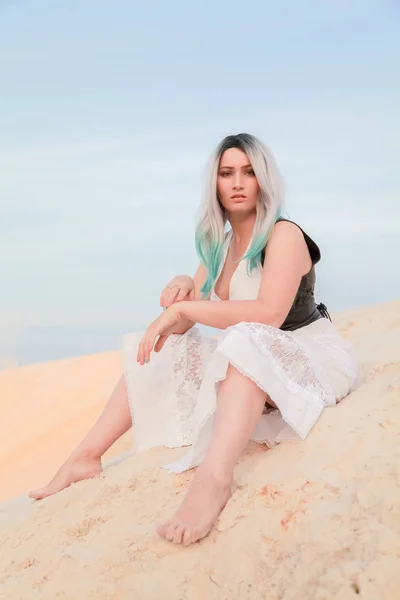 Jovem mulher branca bonita em vestido branco e colete de couro marrom posando na paisagem do deserto com areia . — Fotografia de Stock