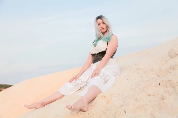 Jeune belle femme caucasienne en robe blanche et gilet en cuir marron posant dans un paysage désertique avec du sable . — Photo