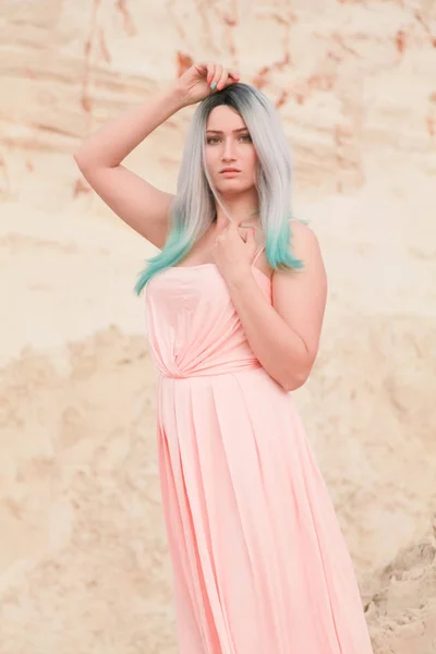 Jeune belle femme caucasienne en robe rose longue posant dans un paysage désertique avec du sable . — Photo