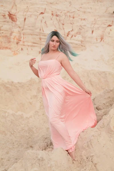 Jeune belle femme caucasienne en robe rose longue posant dans un paysage désertique avec du sable . — Photo