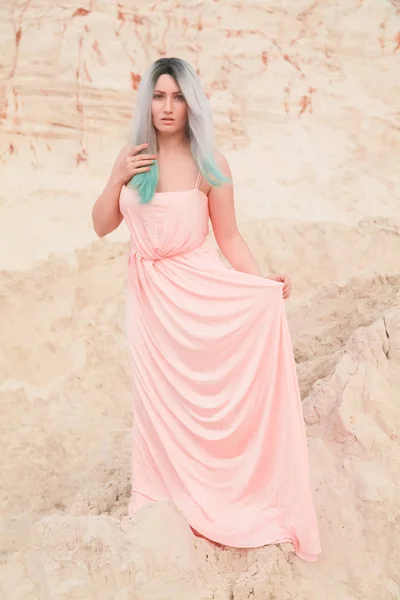 Mulher branca bonita nova no vestido rosa longo posando na paisagem do deserto com areia . — Fotografia de Stock