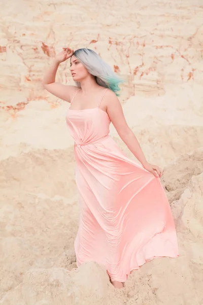 Jeune belle femme caucasienne en robe rose longue posant dans un paysage désertique avec du sable . — Photo