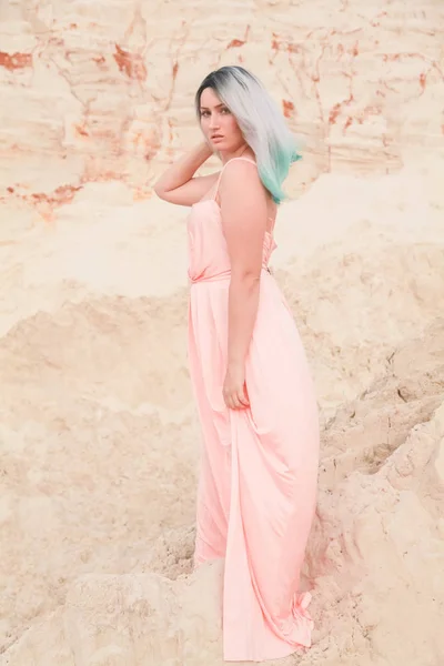 Jeune belle femme caucasienne en robe rose longue posant dans un paysage désertique avec du sable . — Photo