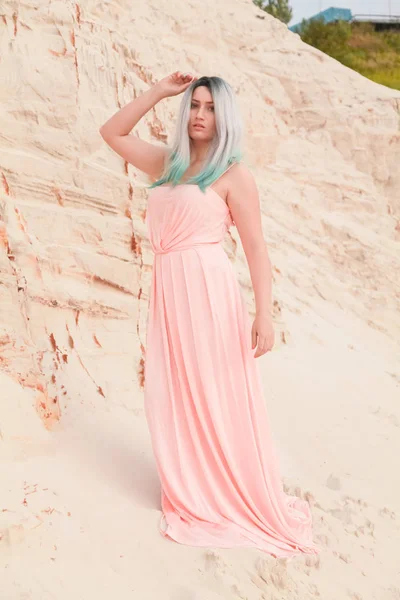 Jonge mooie blanke vrouw in lange roze jurk poseren in woestijn landschap met zand. — Stockfoto
