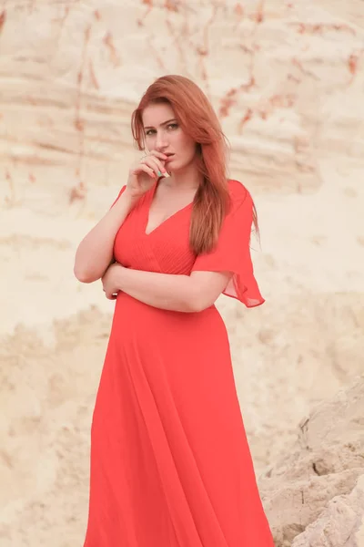 Giovane bella donna caucasica in abito lungo rosso in posa nel paesaggio desertico con sabbia . — Foto Stock