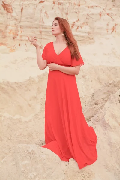 Mulher branca bonita nova no vestido vermelho longo posando na paisagem do deserto com areia . — Fotografia de Stock