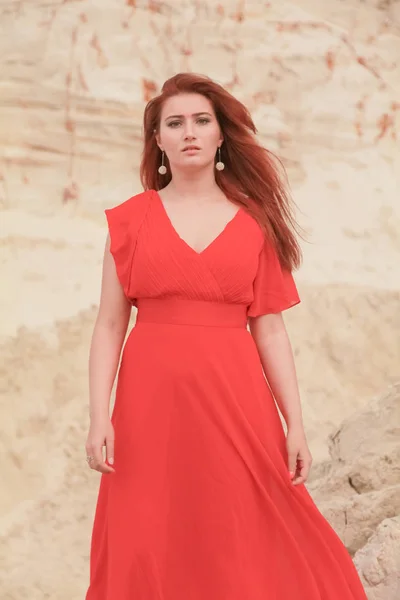 Jeune belle femme caucasienne en robe rouge longue posant dans un paysage désertique avec du sable . — Photo
