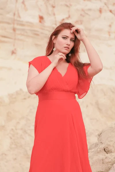 Jeune belle femme caucasienne en robe rouge longue posant dans un paysage désertique avec du sable . — Photo