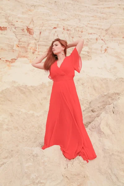 Молодая красивая белая женщина в длинном красном платье позирует в пустыне пейзаж с песком . — стоковое фото