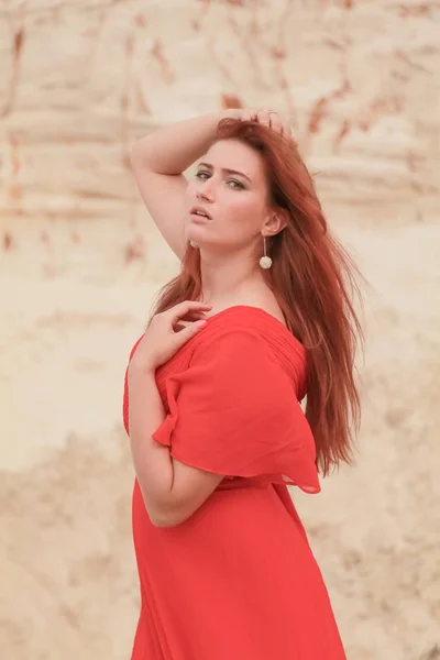 Junge schöne kaukasische Frau im langen roten Kleid posiert in Wüstenlandschaft mit Sand. — Stockfoto