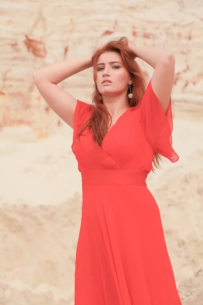 Fiatal gyönyörű kaukázusi nő, hosszú piros ruhában pózol a sivatagban táj homokkal. — Stock Fotó