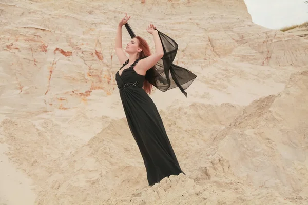 Молодая красивая белая женщина в черном шифонском платье позирует в пустыне пейзаж с песком . — стоковое фото
