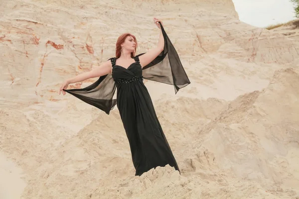 Молодая красивая белая женщина в черном шифонском платье позирует в пустыне пейзаж с песком . — стоковое фото