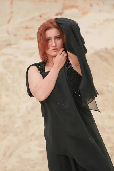Νέα όμορφη καυκάσιος γυναίκα σε μαύρο σιφόν φόρεμα που ποζάρει σε τοπίο έρημο με άμμο. — Φωτογραφία Αρχείου