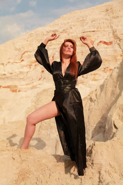 Jeune belle femme caucasienne en robe longue sexy noire posant dans un paysage désertique avec du sable . — Photo