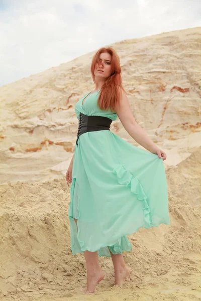 Jeune belle femme caucasienne en robe longue shiffon bleue posant dans un paysage désertique avec du sable . — Photo