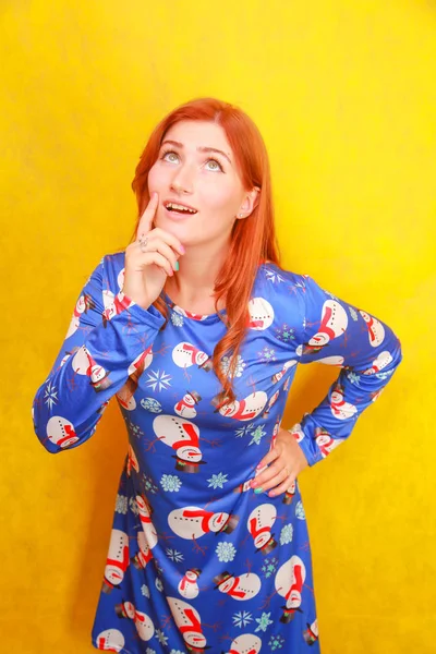 Sarı parlak stüdyo arka plan üzerinde mavi komik noel elbisesi giyen kırmızı saçlı dikkatsiz rüya gibi çekici bayan