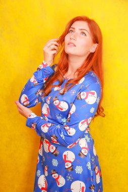 Sarı parlak stüdyo arka plan üzerinde mavi komik noel elbisesi giyen kırmızı saçlı dikkatsiz rüya gibi çekici bayan