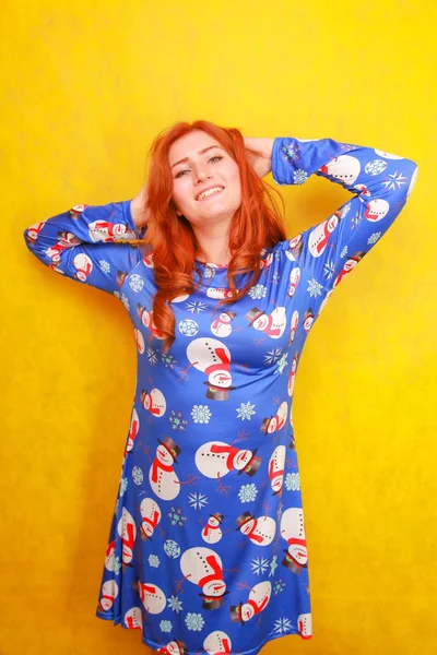 Sarı parlak stüdyo arka plan üzerinde mavi komik noel elbisesi giyen kırmızı saçlı dikkatsiz rüya gibi çekici bayan