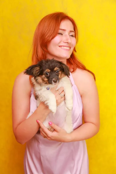 노란색 배경에 강아지를 포용 편안한 빨간 머리 소녀. 개와 함께 차가운 흰색 매력 여성의 스튜디오 초상화. — 스톡 사진