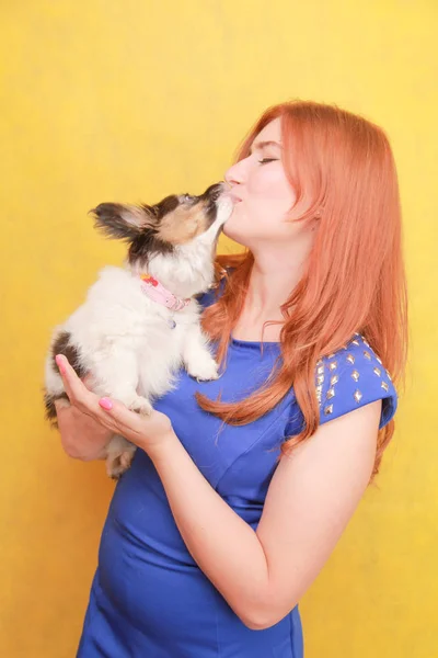 Расслабленная рыжая девушка обнимает щенка на жёлтом фоне. Студийный портрет белой привлекательной женщины, отдыхающей с собакой . — стоковое фото
