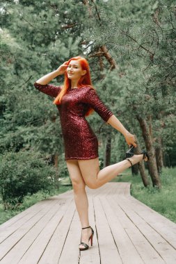 kiraz rengi gece elbisesi kırmızı saçlı kadın şehir parkı arka planda yürüyüş ve yaz keyfini çıkarın