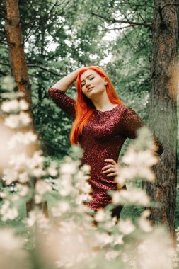 kiraz rengi gece elbisesi kırmızı saçlı kadın şehir parkı arka planda yürüyüş ve yaz keyfini çıkarın