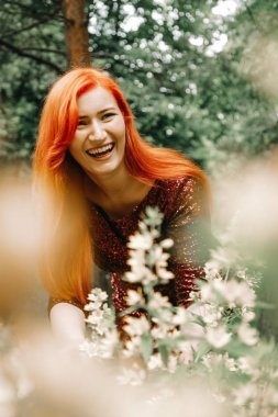 kiraz rengi gece elbisesi kırmızı saçlı kadın şehir parkı arka planda yürüyüş ve yaz keyfini çıkarın