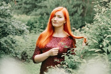 kiraz rengi gece elbisesi kırmızı saçlı kadın şehir parkı arka planda yürüyüş ve yaz keyfini çıkarın