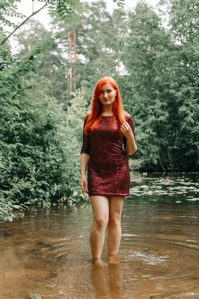 Mulher de cabelos vermelhos em cor de cereja vestido de noite andando no parque da cidade fundo e desfrutar de verão — Fotografia de Stock