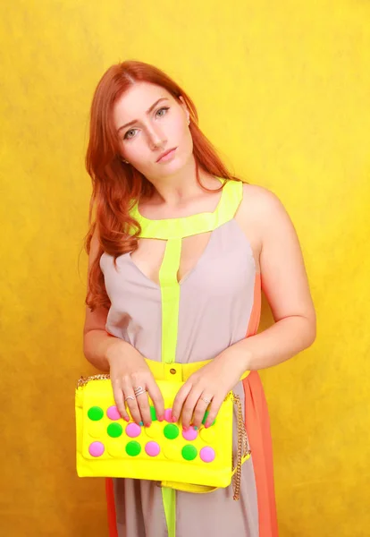 Красивая рыжая девушка в ярком летнем платье с желтой яркой кожаной сумкой — стоковое фото