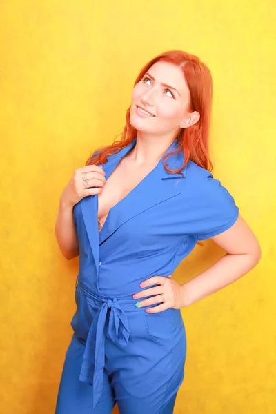 Bonita mujer de pelo rojo en la moda azul en general de pie sobre fondo amarillo — Foto de Stock