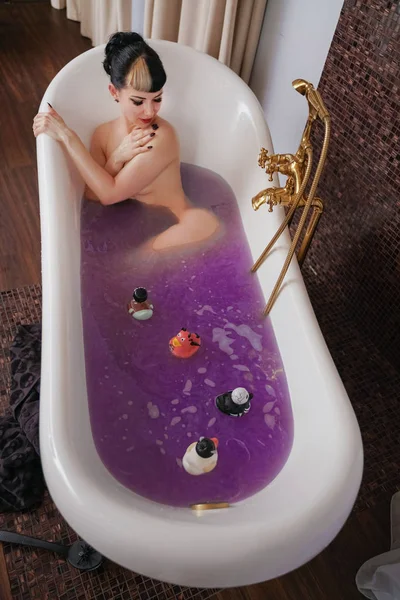 Healthy naked goth girl with black hair in the luxury brown bathroom with purple salt water — Stock Photo, Image