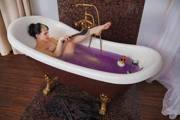 Healthy naked goth girl with black hair in the luxury brown bathroom with purple salt water — Stock Photo, Image