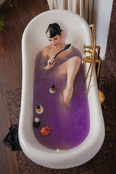 Gothique nue saine fille aux cheveux noirs dans la salle de bain marron de luxe avec de l'eau salée violette — Photo