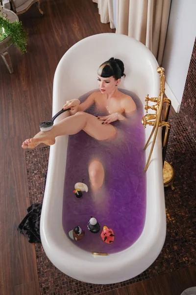 Gesunde nackte Gothic-Mädchen mit schwarzen Haaren im luxuriösen braunen Badezimmer mit lila Salzwasser — Stockfoto