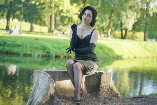 Außenporträt eines Pinup-Girls auf Baumstumpf im Stadtpark am Wasser — Stockfoto