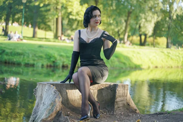 Portrait extérieur de pinup girl assis sur souche dans le parc de la ville près de l'eau — Photo