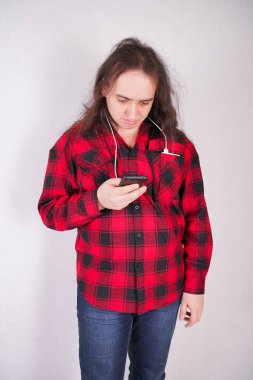 Stüdyo'da beyaz bir arka plan üzerinde bir telefon ile ekose kırmızı gömlek uzun saçlı nerd adam