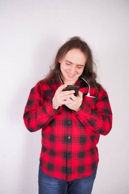 Stüdyo'da beyaz bir arka plan üzerinde bir telefon ile ekose kırmızı gömlek uzun saçlı nerd adam