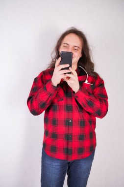 Stüdyo'da beyaz bir arka plan üzerinde bir telefon ile ekose kırmızı gömlek uzun saçlı nerd adam