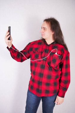 Stüdyo'da beyaz bir arka plan üzerinde bir telefon ile ekose kırmızı gömlek uzun saçlı nerd adam