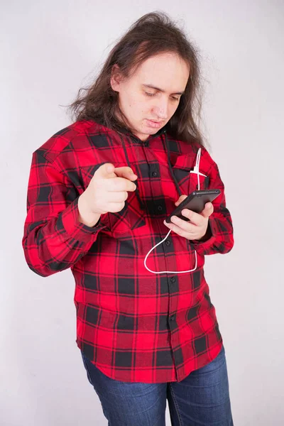 Hombre nerd de pelo largo en una camisa roja a cuadros con un teléfono sobre un fondo blanco en el estudio — Foto de Stock