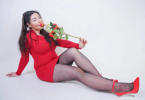 Bastante mezcla corrió más tamaño chica en vestido midi rojo elegante sentado en fondo blanco estudio con rosa roja —  Fotos de Stock