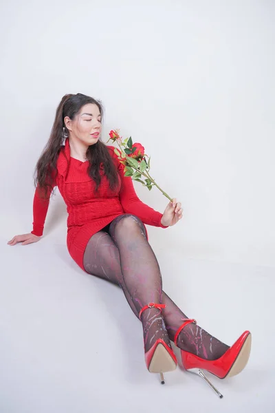 Bastante mezcla corrió más tamaño chica en vestido midi rojo elegante sentado en fondo blanco estudio con rosa roja —  Fotos de Stock