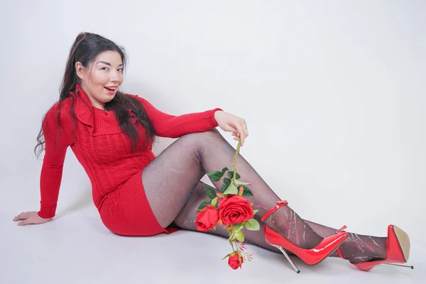 Bastante mezcla corrió más tamaño chica en vestido midi rojo elegante sentado en fondo blanco estudio con rosa roja —  Fotos de Stock